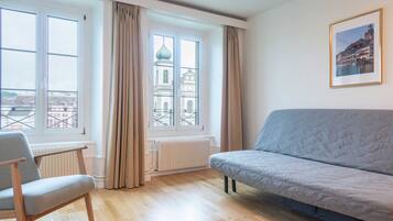 Una habitación con sofá, sillón, radiador y ventana con cortinas.