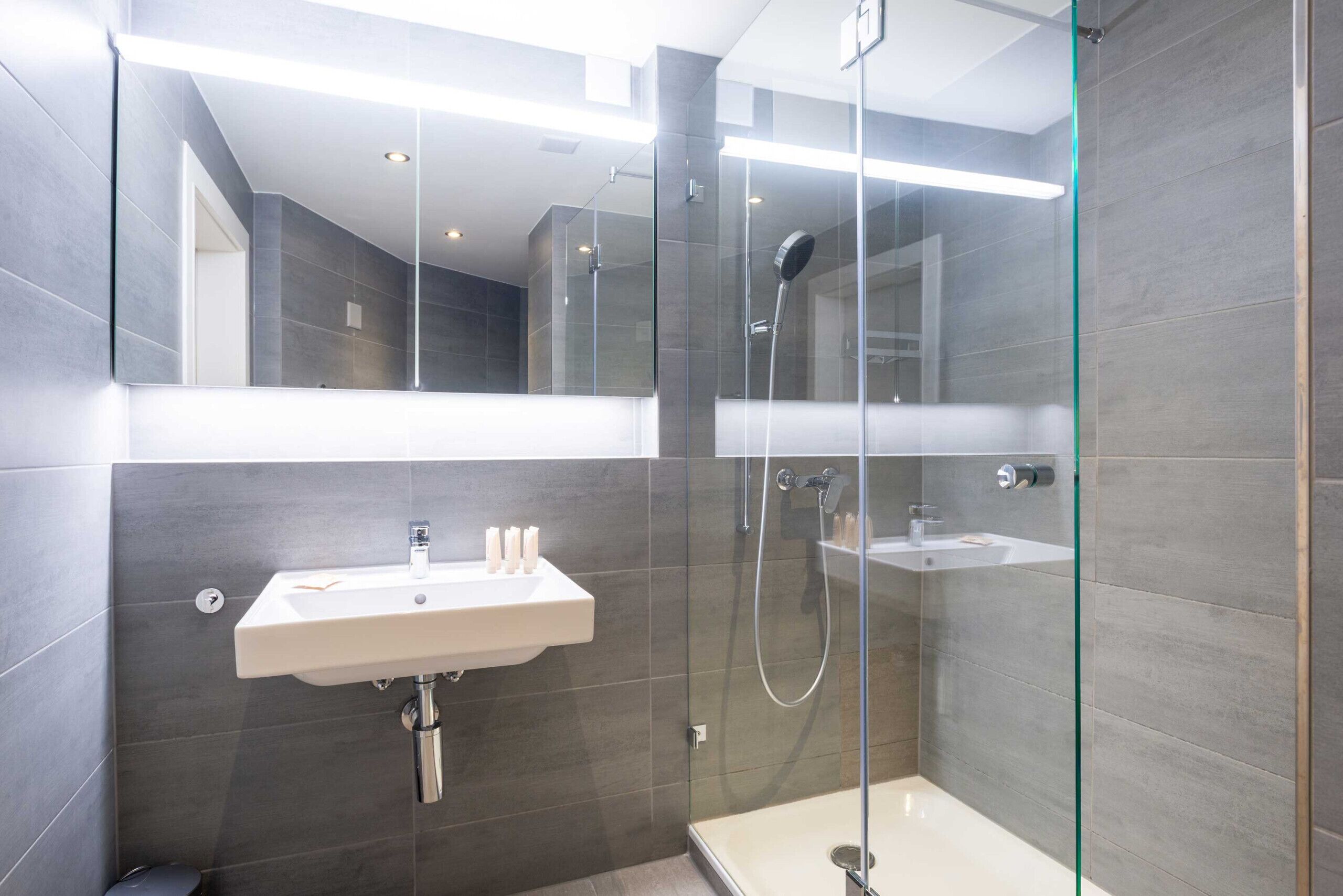 Une salle de bain moderne avec une douche en verre, un lavabo blanc et un miroir au-dessus du lavabo.