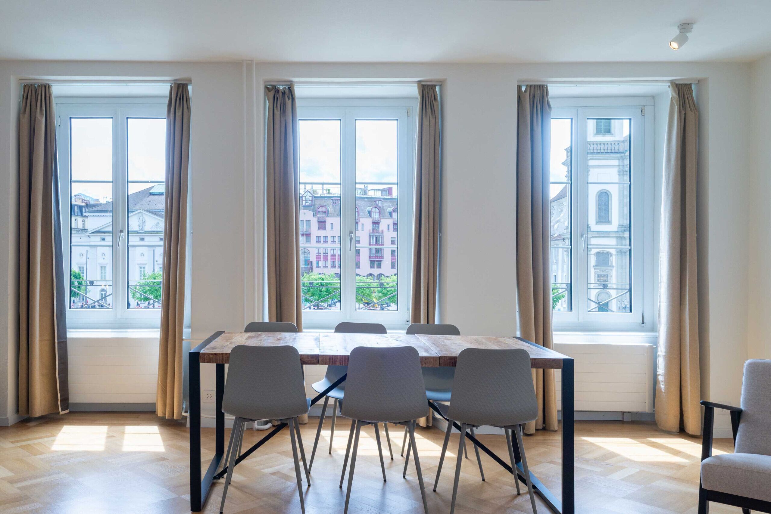 Ein Konferenzraum mit einem großen Tisch, sechs Stühlen und drei fensterbepflanzten Fenstern.