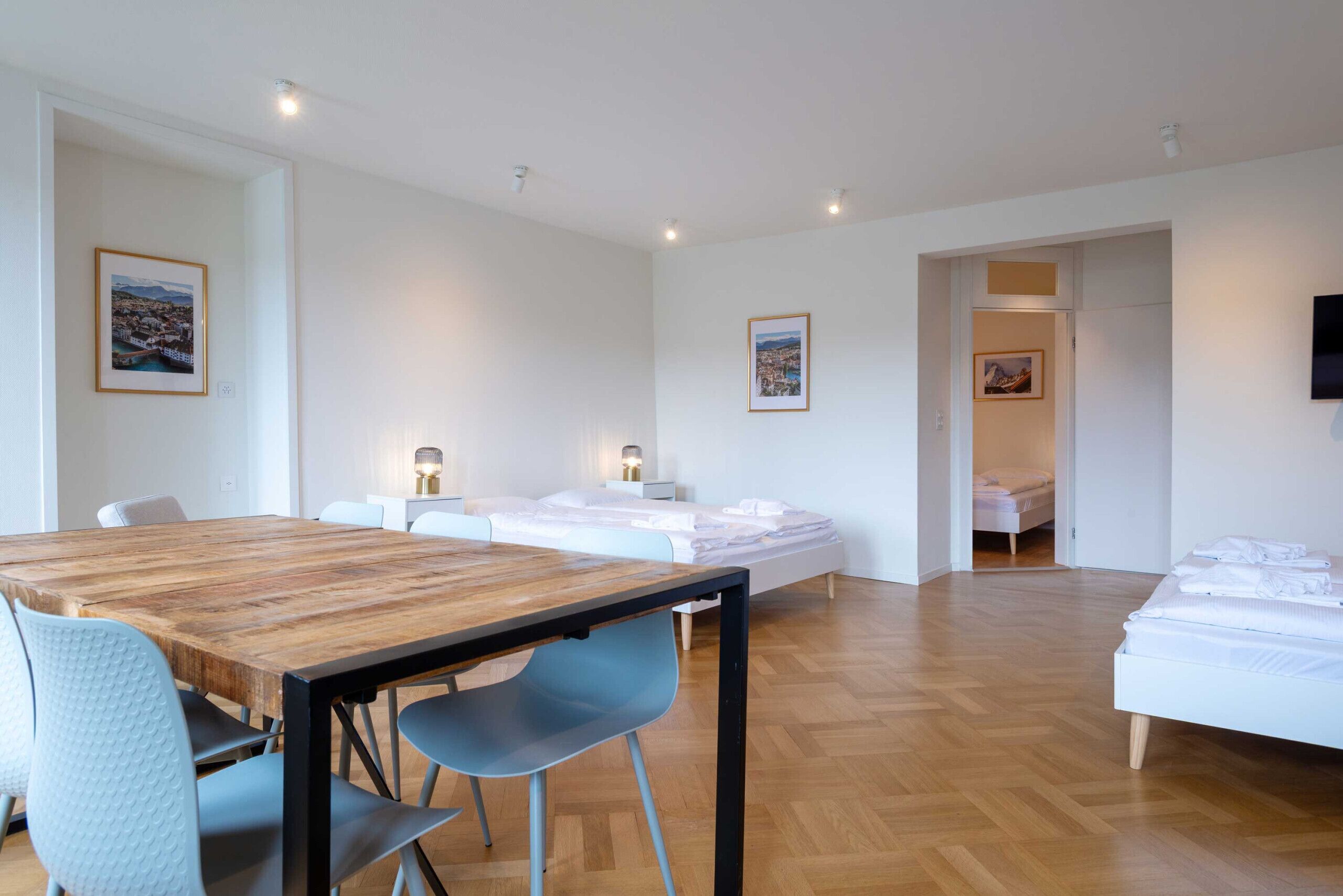 Una habitación moderna con una mesa de madera, dos camas y un televisor montado en la pared.