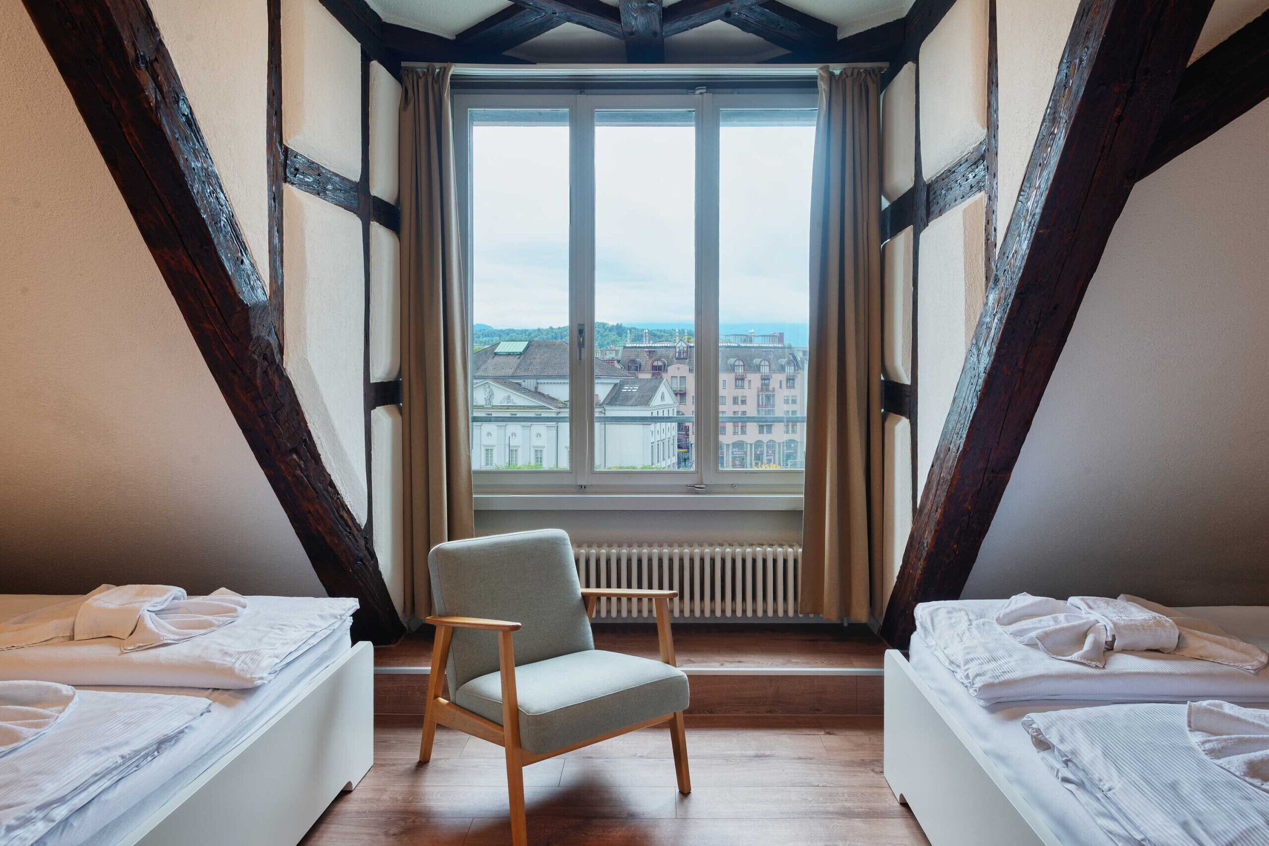 Ein Zimmer mit großem Fenster, einem Sessel und zwei Betten.