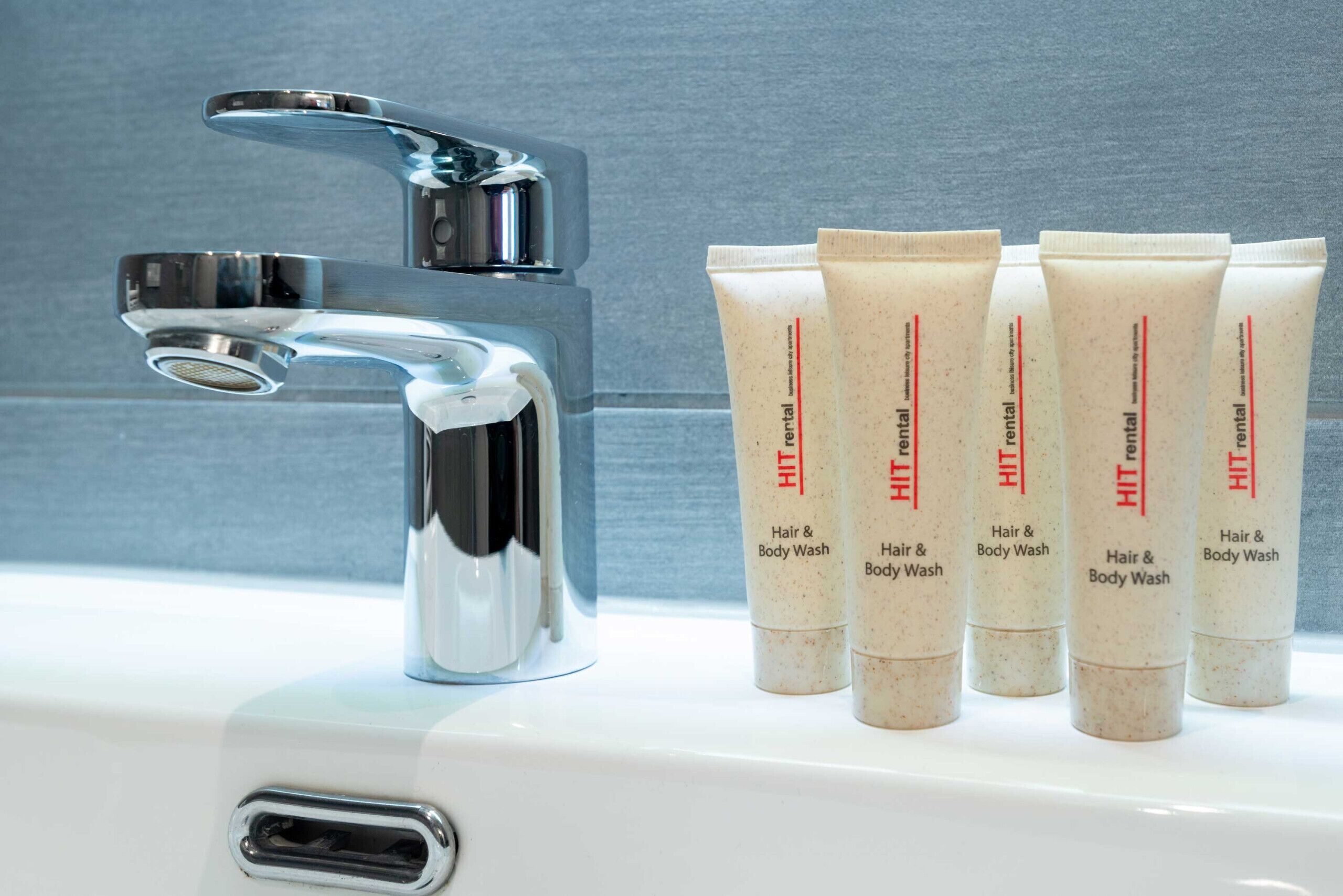 A bathroom sink with a chrome faucet and five tubes of Hit hair and body wash.