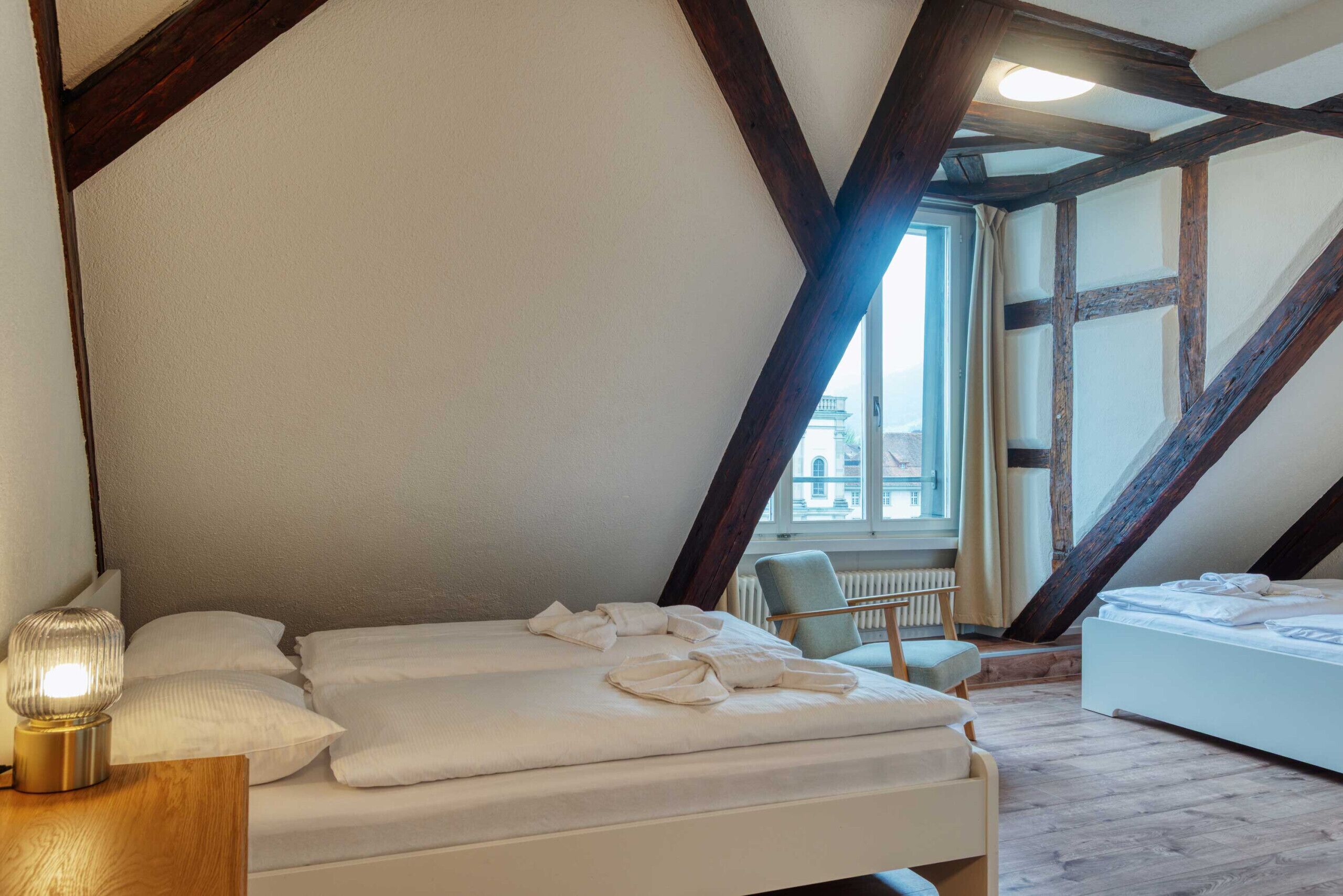 A bedroom with a sloped ceiling, a bed, a chair, and a lamp.