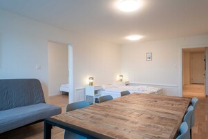 Una habitación moderna con una mesa de comedor de madera, un sofá gris y una cama con ropa de cama blanca.