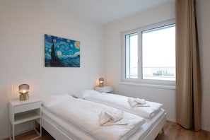 A room with two beds, a painting on the wall, and a window with curtains.