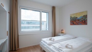 A hotel room with a large window, a bed, a bedside table with a lamp, and a painting on the wall. - Hitrental Hohlstrasse Apartments (Zürich)