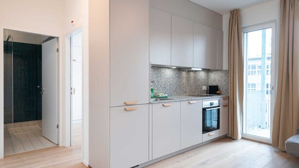 A modern kitchen with white cabinets, a granite countertop, and a built-in oven. - Hitrental Hohlstrasse Apartments (Zürich)