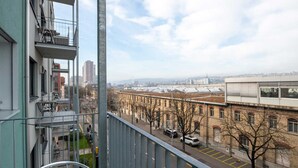 A view from a balcony overlooking a street with parked cars, a building with a brick facade, and a clear sky. - Hitrental Hohlstrasse Apartments (Zürich)