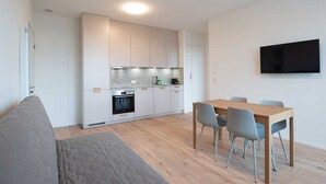 A modern kitchen with white cabinets, a built-in oven, and a dining area with a wooden table and chairs. - Hitrental Hohlstrasse Apartments (Zürich)