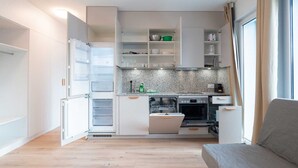 A compact kitchen with white cabinets, a built-in oven, and a dining area with a sofa. - Hitrental Hohlstrasse Apartments (Zürich)