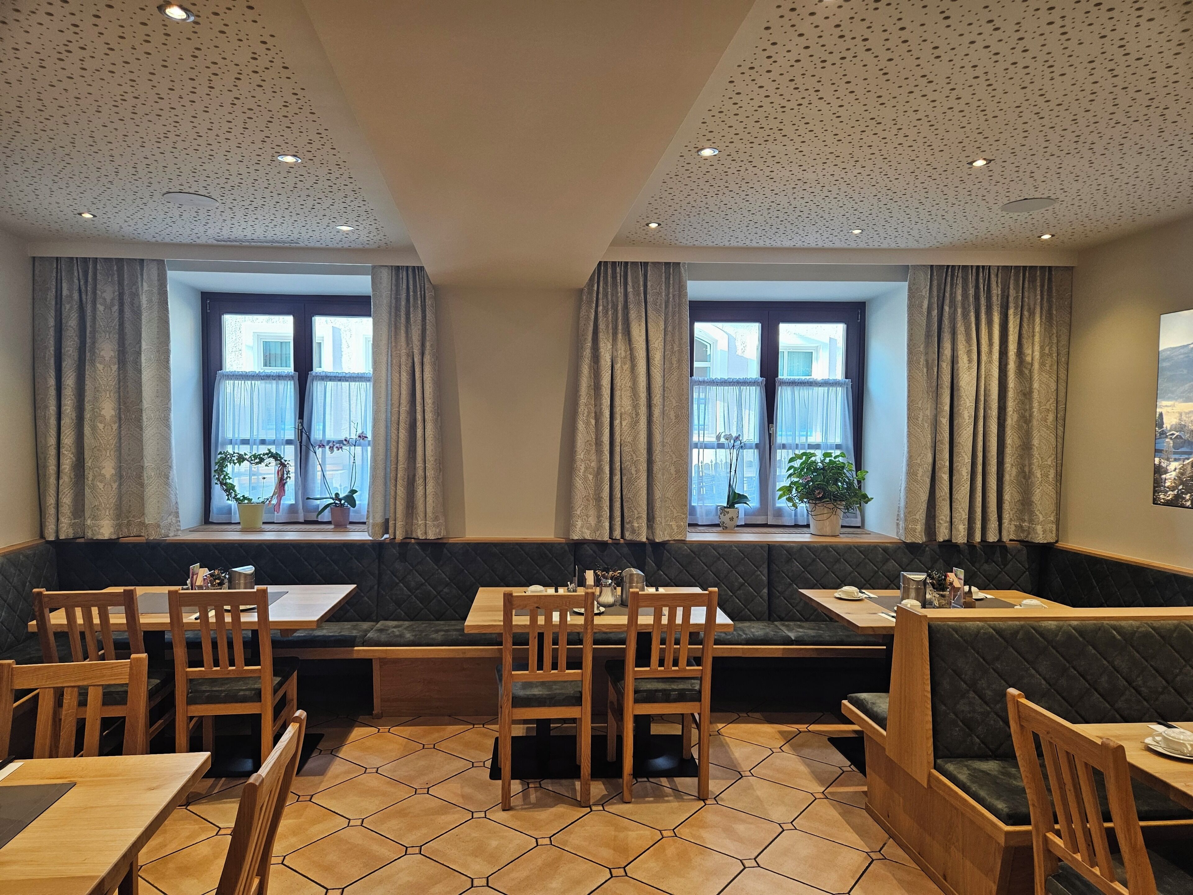 A restaurant with booths and tables, large windows with curtains, and a tiled floor.