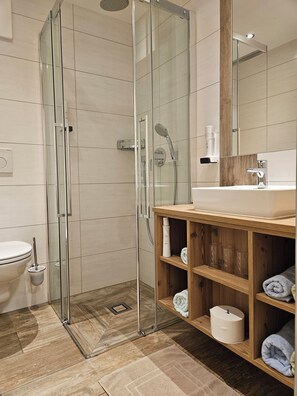 A modern bathroom with a glass-enclosed shower, a wooden vanity with shelves, and a large mirror.
