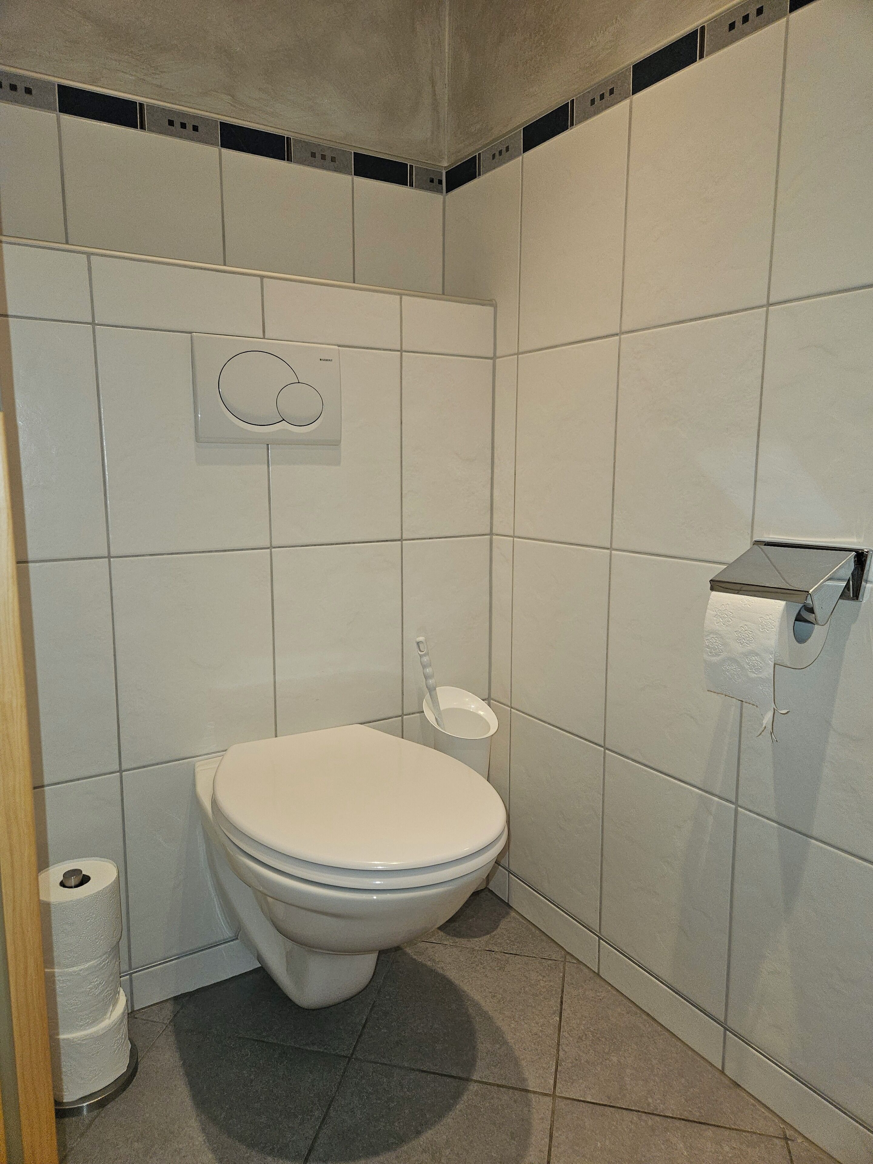 Un baño pequeño y moderno con inodoro, dispensador de papel higiénico y un cubo de basura.