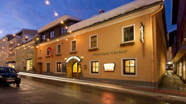 Un hotel con techo nevado, un letrero que dice "Gasthof Lücke" y una calle con estelas de luz que indican movimiento.