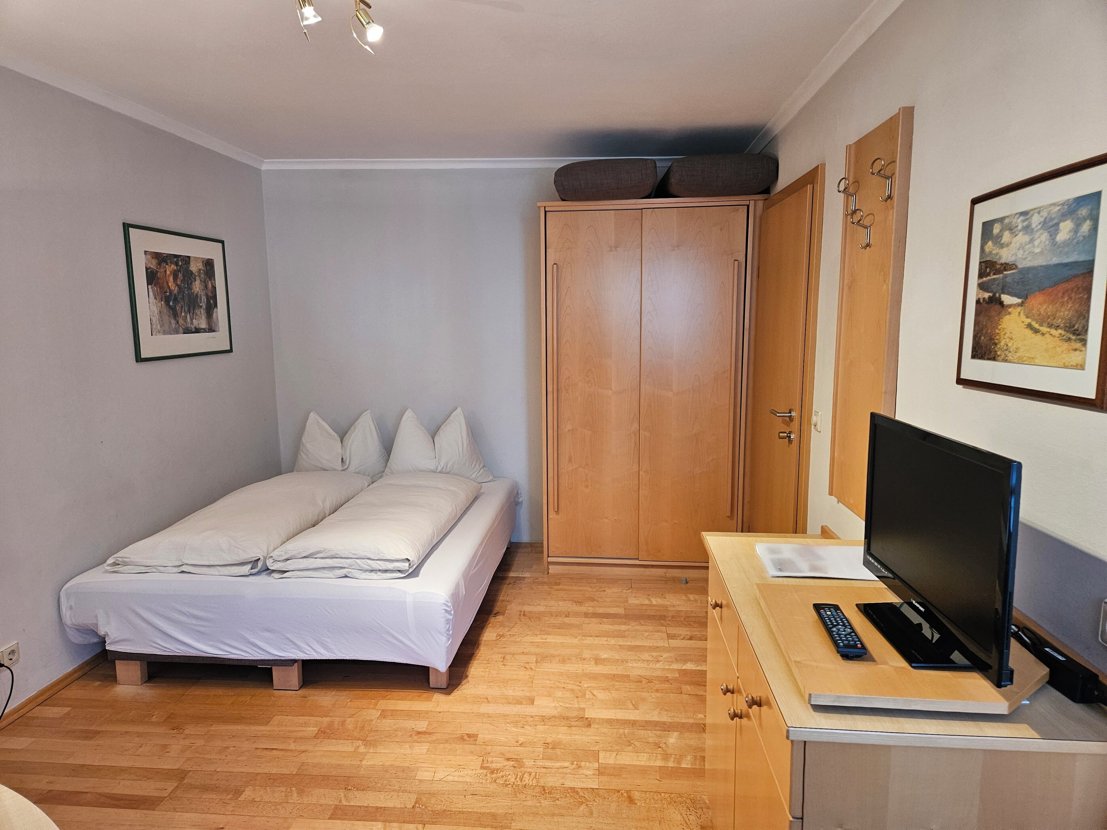 Une chambre à coucher avec un lit, une armoire en bois et un téléviseur posé sur un bureau en bois.