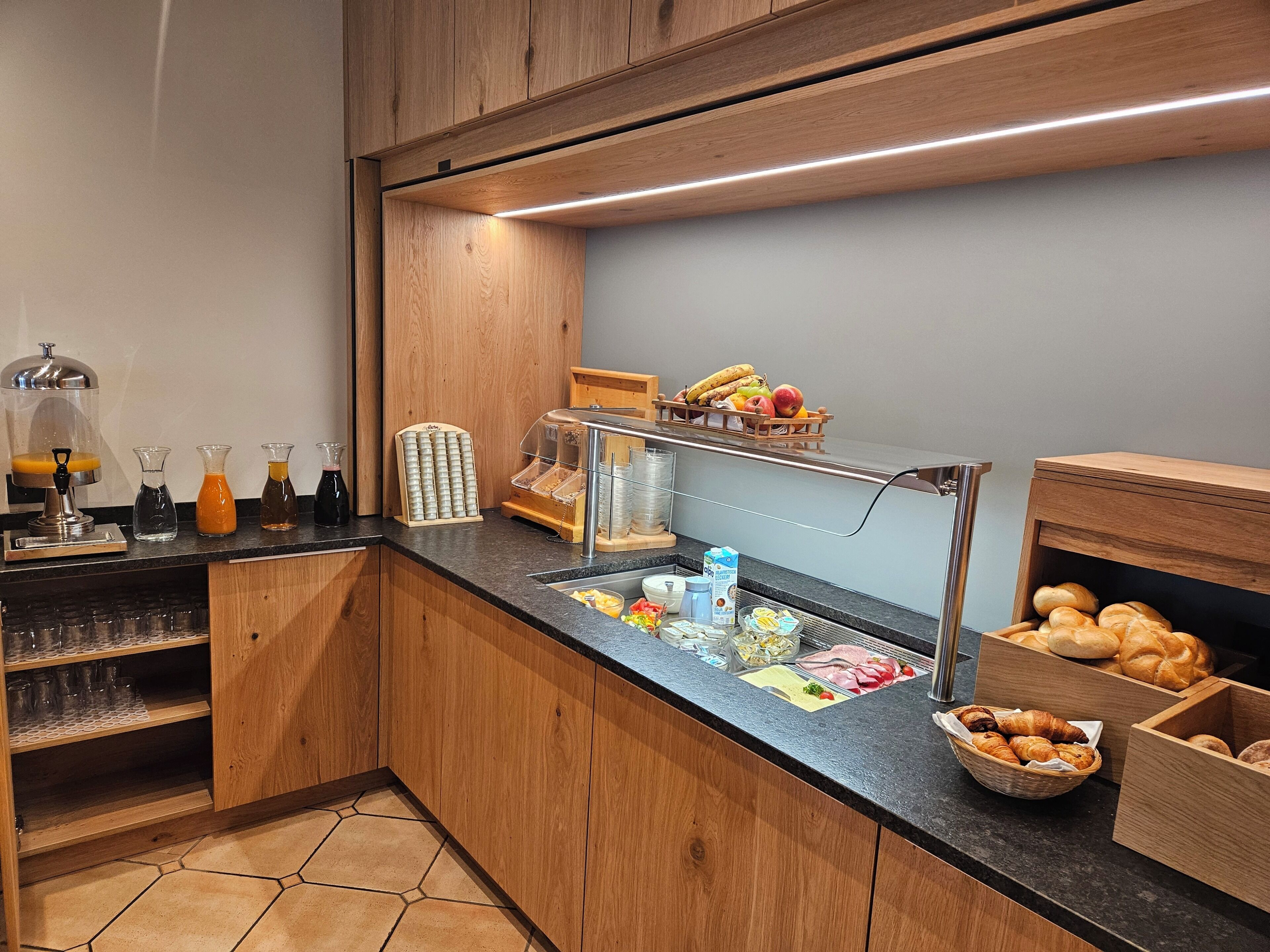 A breakfast bar with a variety of food items, a coffee station, and a fruit display.