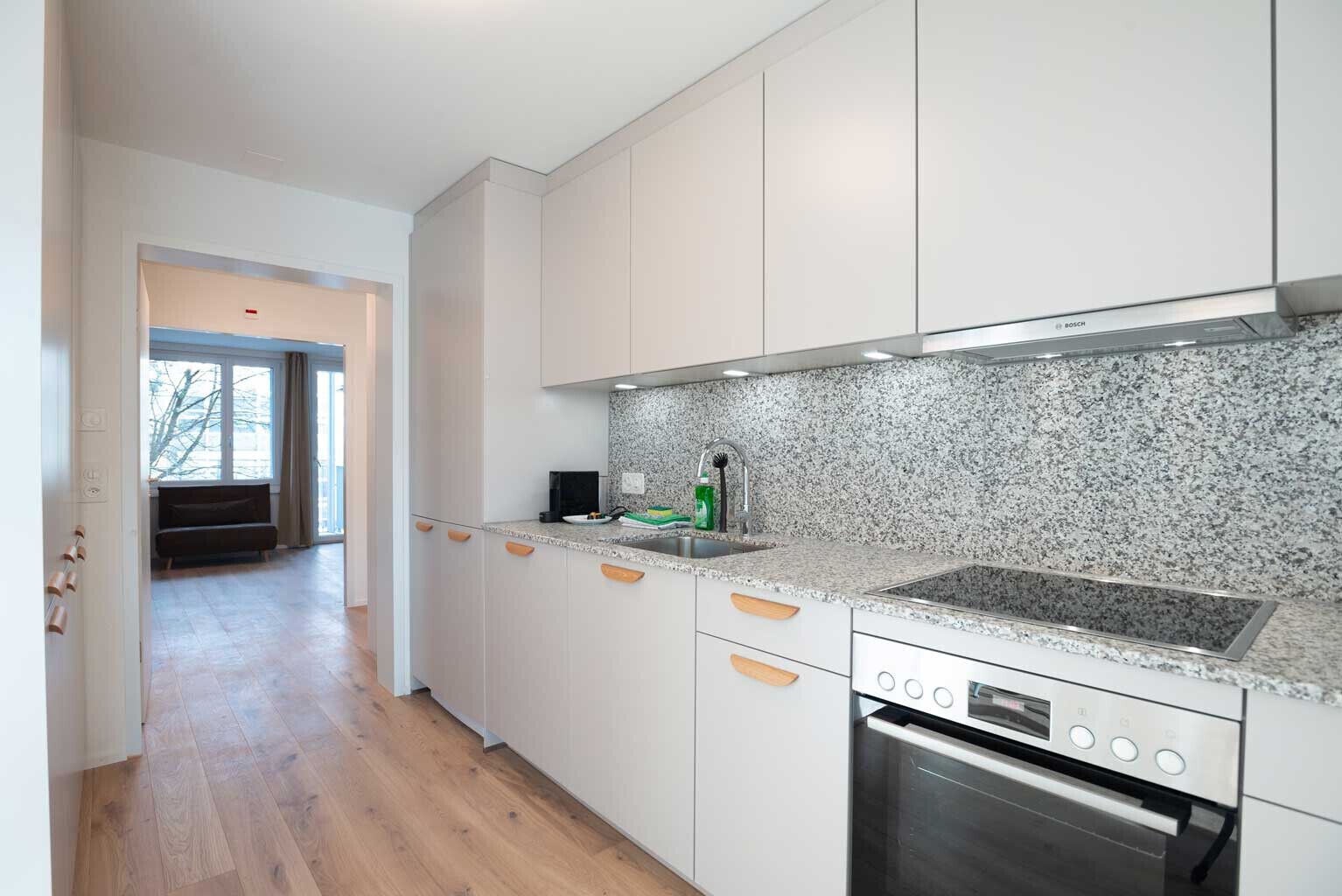 Eine moderne Küche mit weißen Schränken, einer Granitabdeckung und einem Backofen von Bosch.