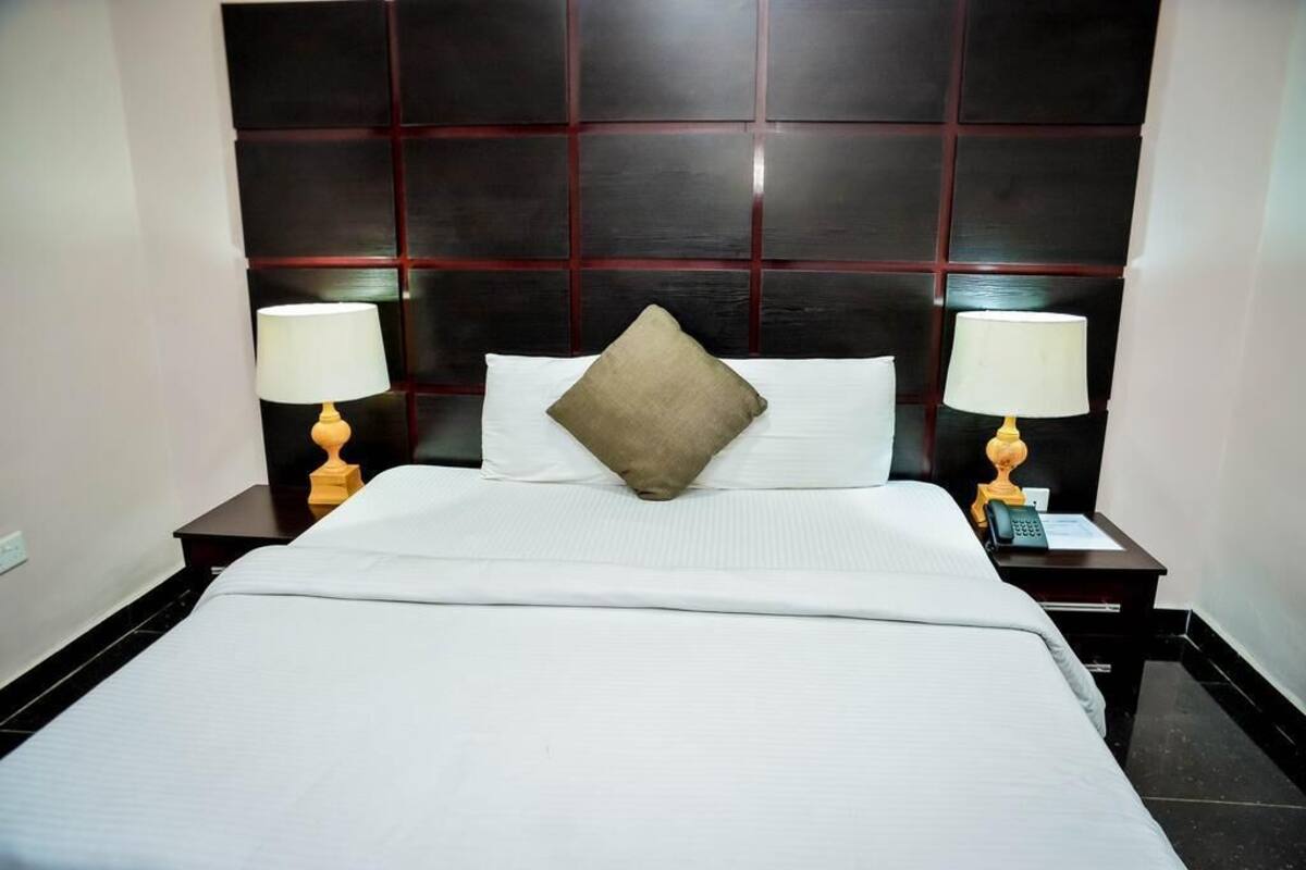 A hotel room with a large bed, two bedside tables with lamps, a dark headboard, and a single decorative pillow.