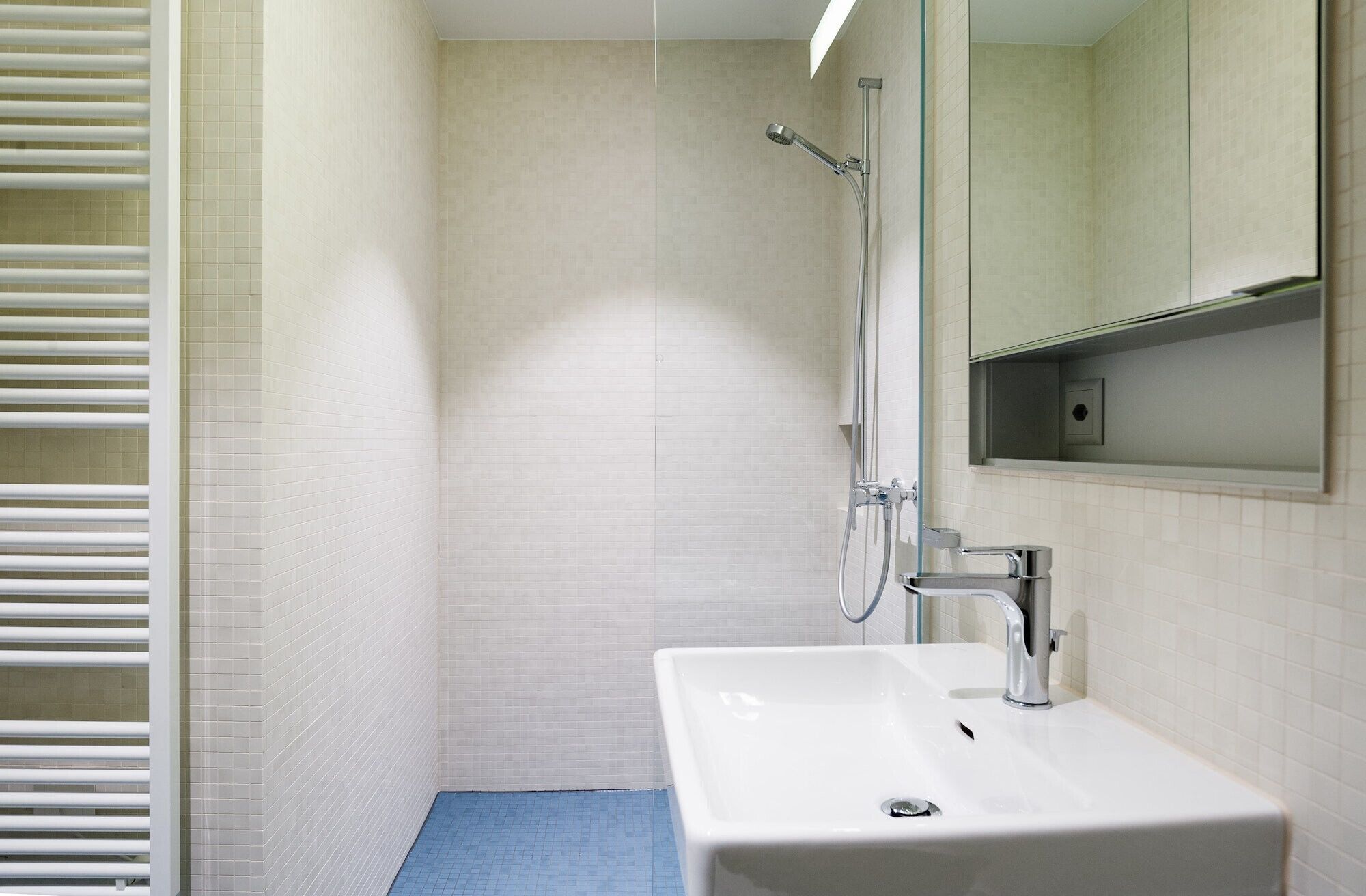 Un baño con lavamanos blanco, un espejo y ducha con cabezal de ducha de mano.