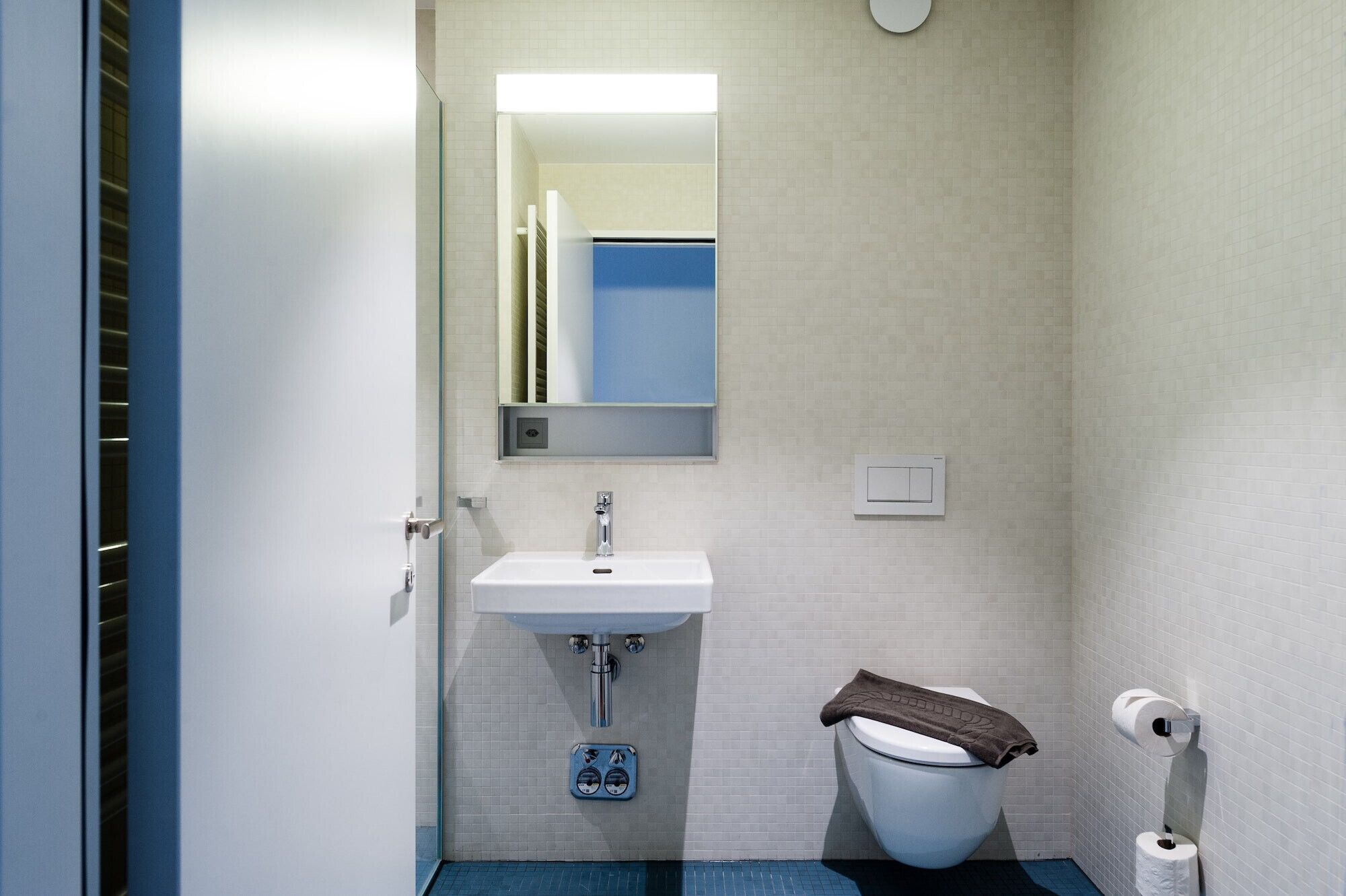 Un baño pequeño con un lavabo blanco, un espejo, un inodoro y un suelo azul.