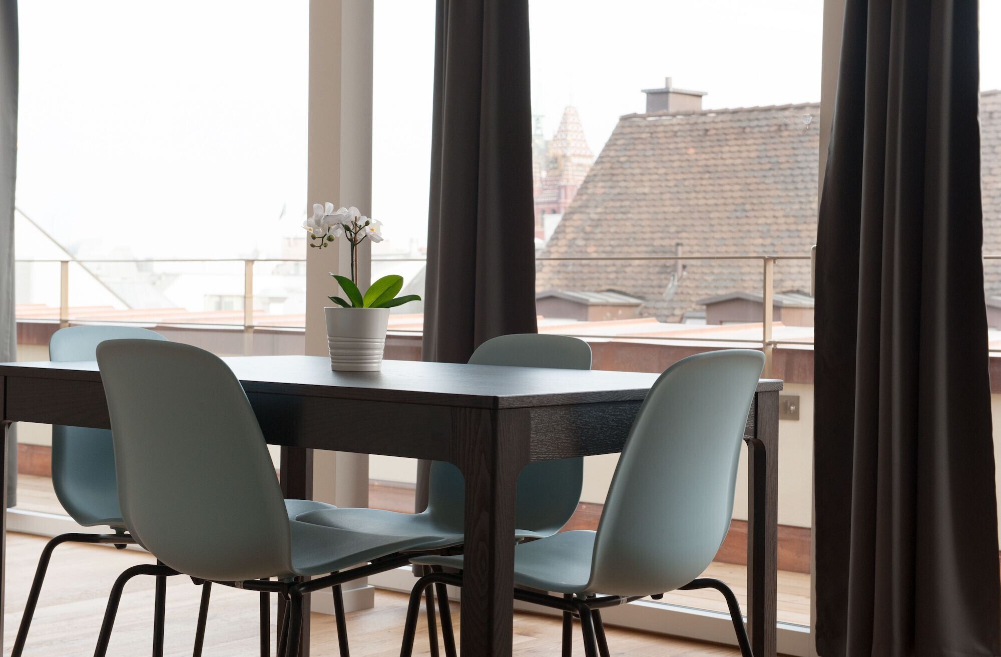 A dining area with a table and chairs, a potted plant, and a view of buildings through large windows.