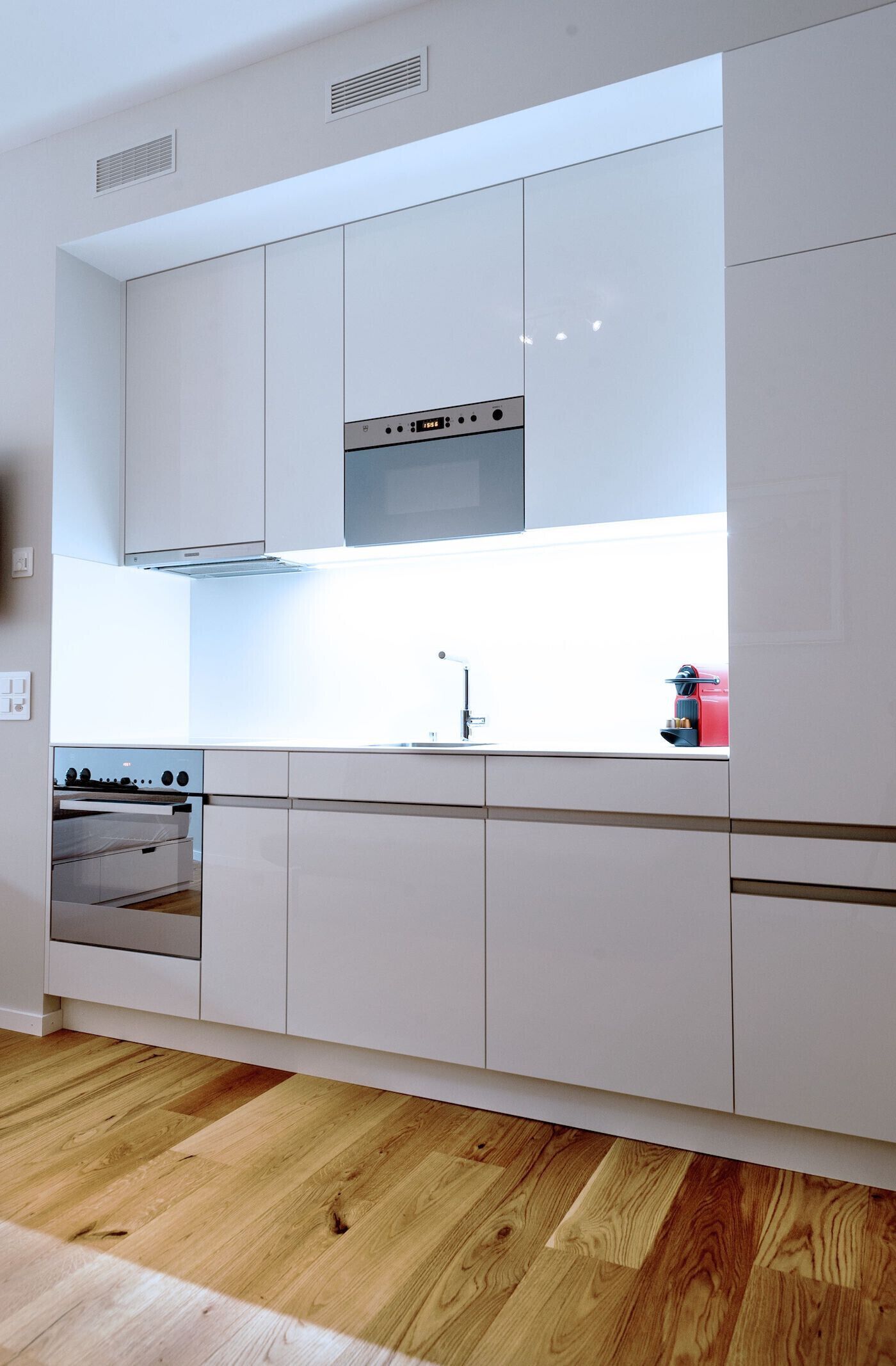 A modern kitchen with white cabinets, a stainless steel range hood, and a built-in oven.