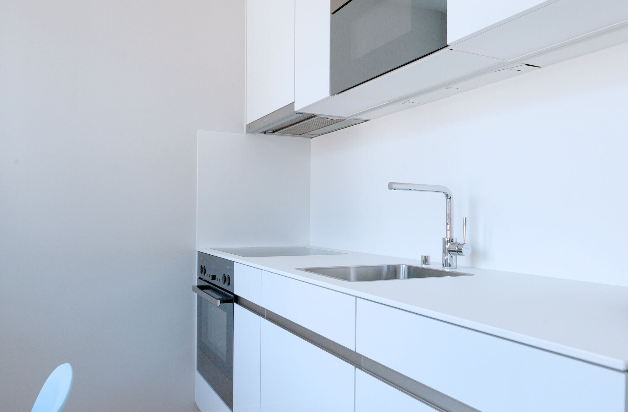 Una cocina moderna con armarios blancos, un lavamanos de acero inoxidable y un horno empotrado.