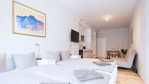 Ett modernt hotellrum med två sängar, ett skrivbord, en stol, en TV och ett litet köksutrymme.
