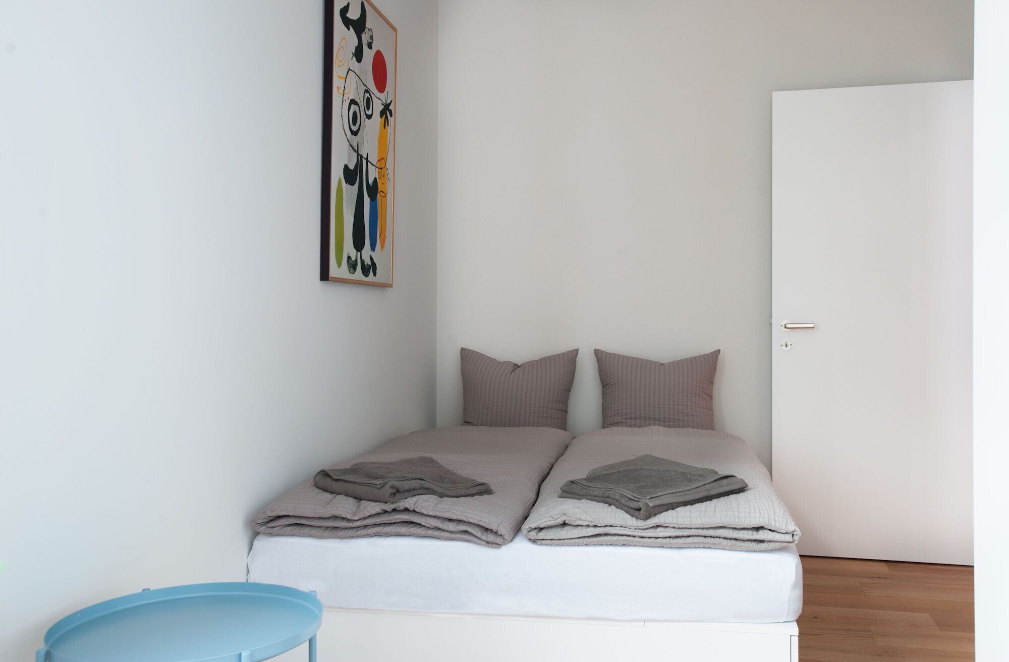 Un dormitorio con cama, almohadas, una silla azul y una puerta.