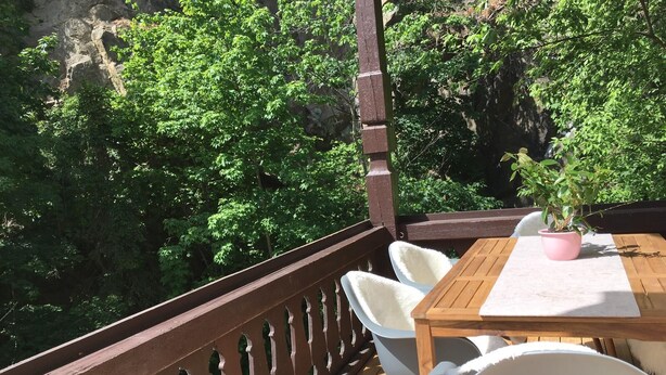 Una terraza de madera con mesa y sillas, con vista a un exuberante bosque verde.