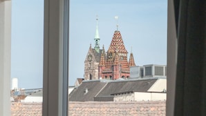Vista a través de una ventana que muestra un edificio con tejado de baldosas y una iglesia característica con aguja verde al fondo.