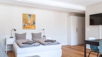 A modern bedroom with a bed, bedside lamps, a painting, a wardrobe, and a TV.