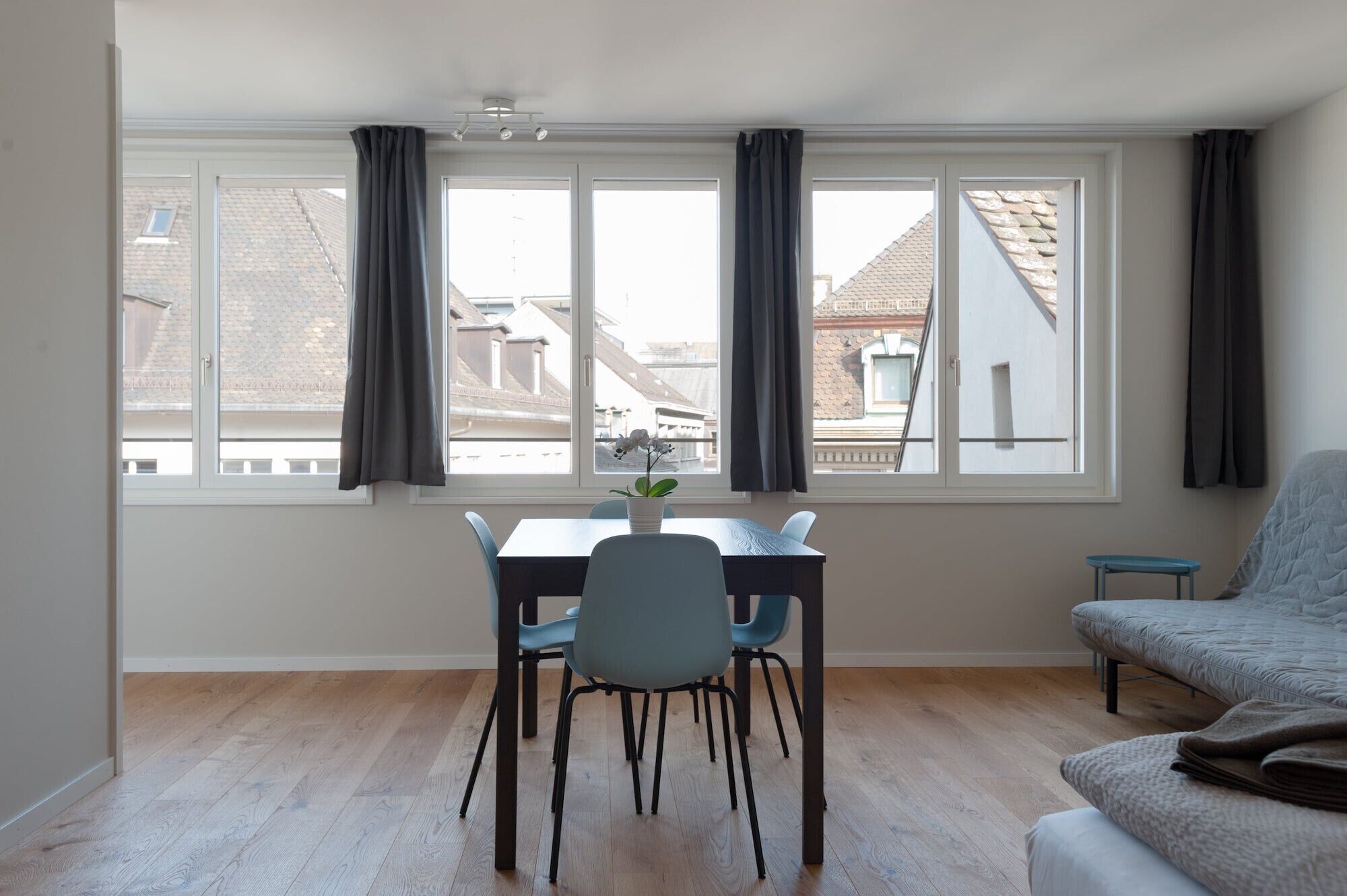Ein Zimmer mit Esstisch, Stühlen, einer Couch und einem großen Fenster mit Vorhängen.