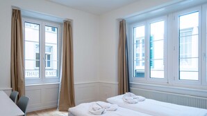 A hotel room with two beds, a desk, and large windows with curtains. - Hitrental Old Town Apartments (Lucerne)