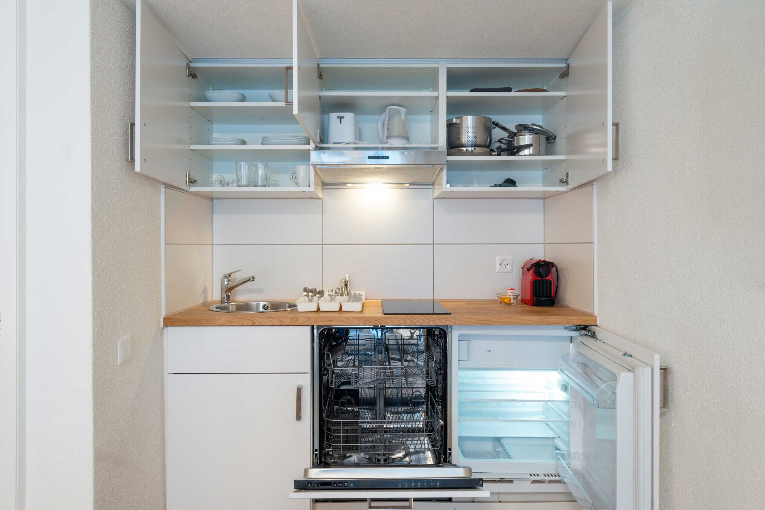 A compact kitchen with a dishwasher, a sink, and open shelving above.