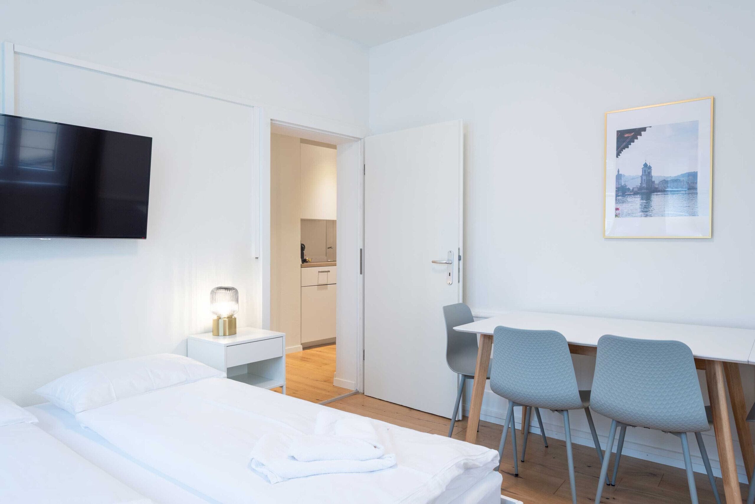 Ein Hotelzimmer mit einem Bett, einem Schreibtisch, zwei Stühlen, einem Fernseher, einer Nachttischlampe und einem gerahmten Bild an der Wand.