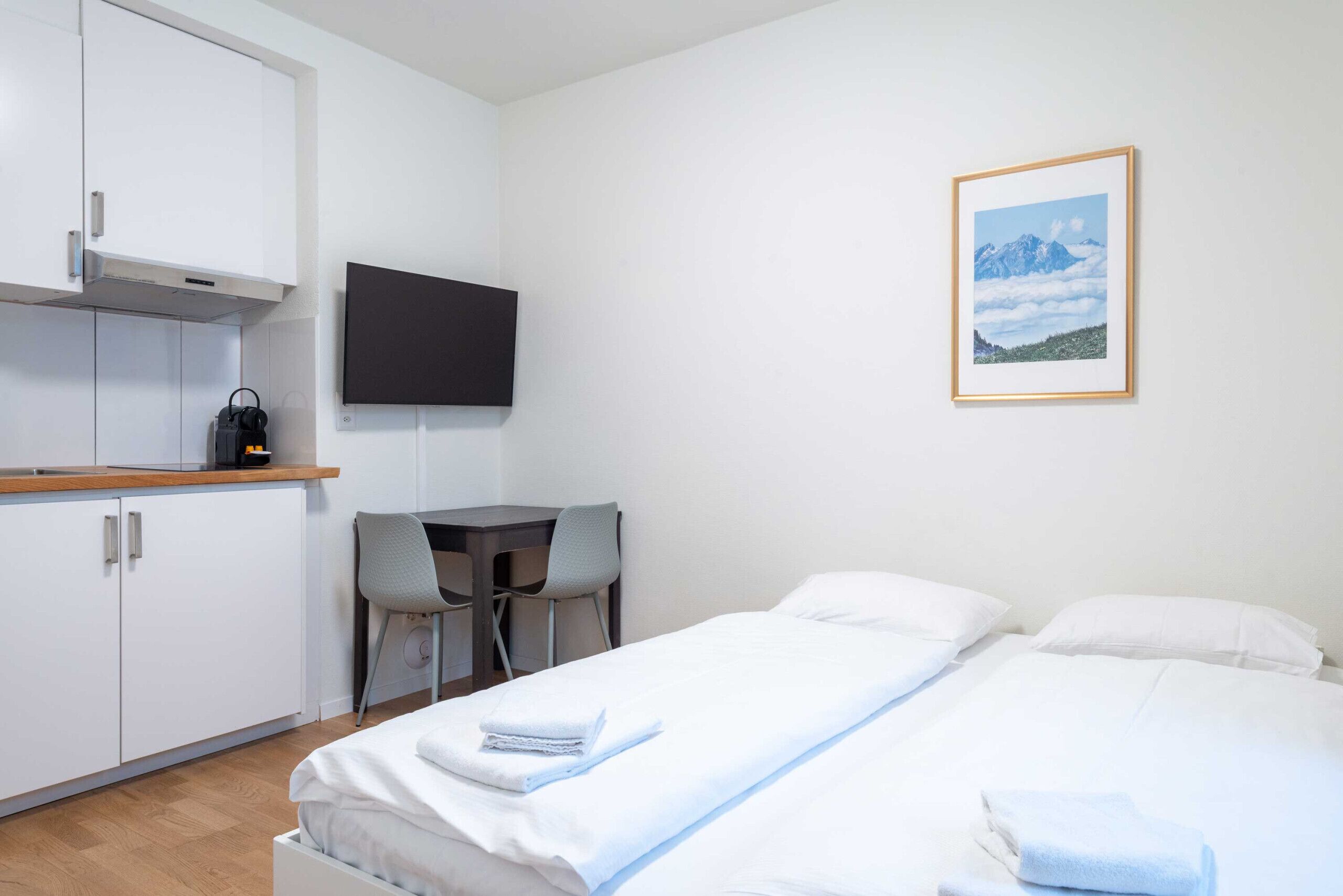 A hotel room with a bed, a desk, a chair, a TV, and a framed picture on the wall.