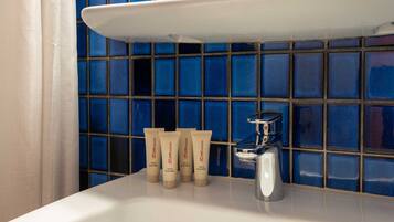A bathroom with a white sink, blue-tiled wall, and three tubes of hair and body wash.