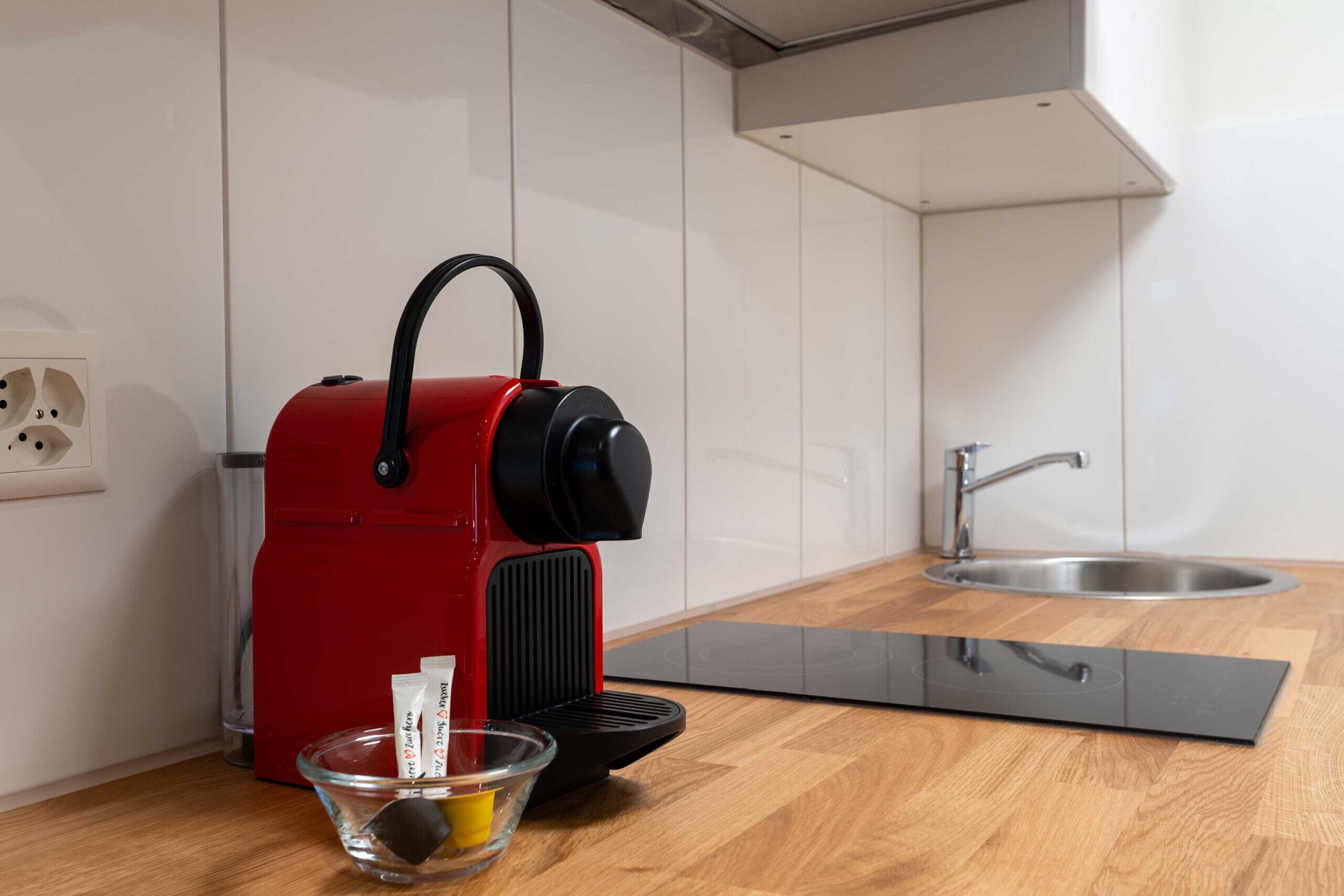 Una cocina con un electrodoméstico rojo, un bol de cristal con un objeto amarillo y una bandeja negra sobre la encimera.