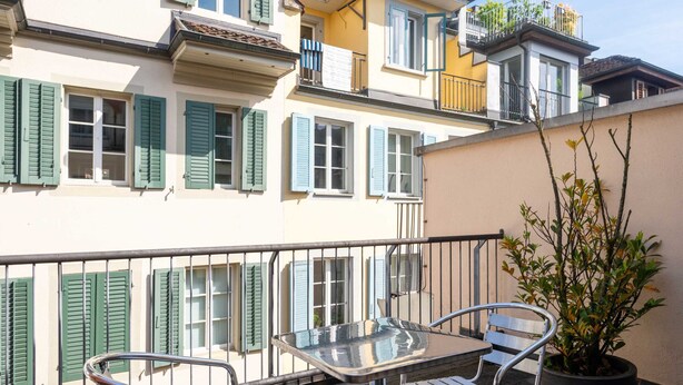 A balcony with a table and chairs, a potted plant, and a building with multiple windows and balconies. - Hitrental Old Town Apartments (Lucerne)