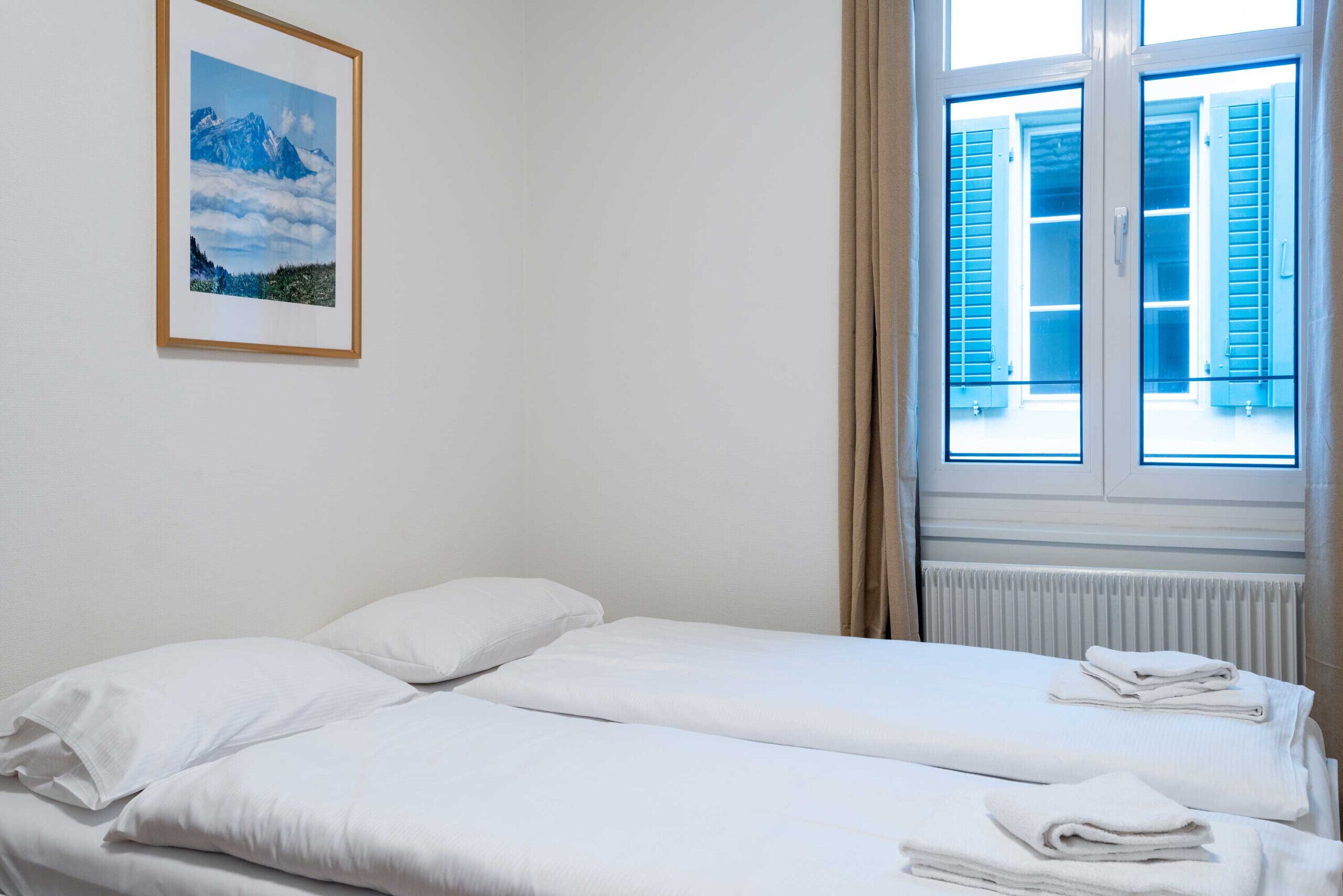 Une chambre avec deux lits, un tableau encadré au mur et une fenêtre avec des volets.