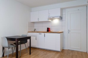 Uma cozinha compacta com armários brancos, bancada de madeira, cafeteira e uma porta.