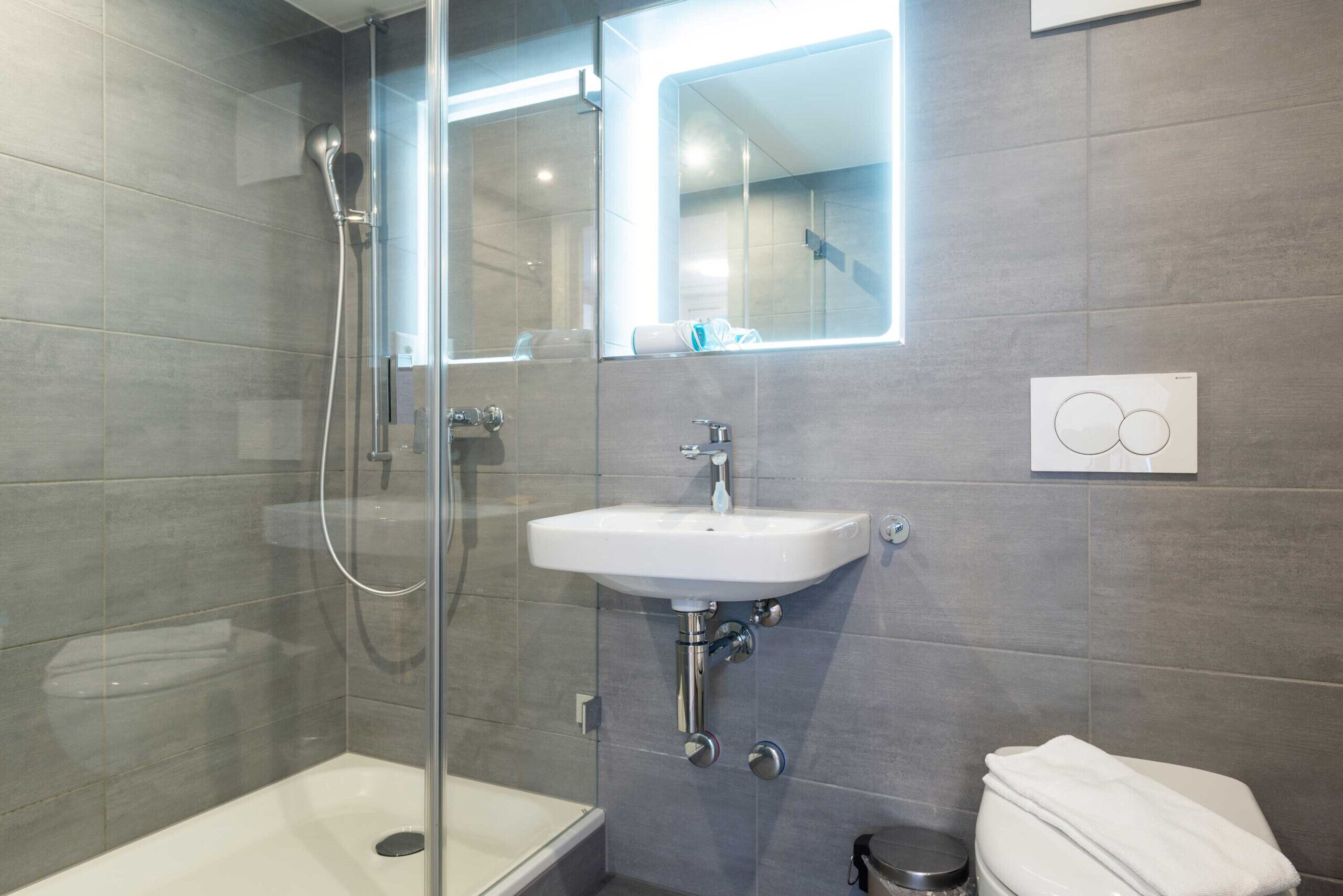 A modern bathroom with a glass-enclosed shower, a white sink, and a toilet.