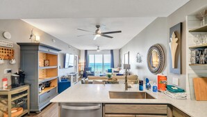 A modern kitchen with a central island, a dining area with a view, and a living room with a sofa and a TV.