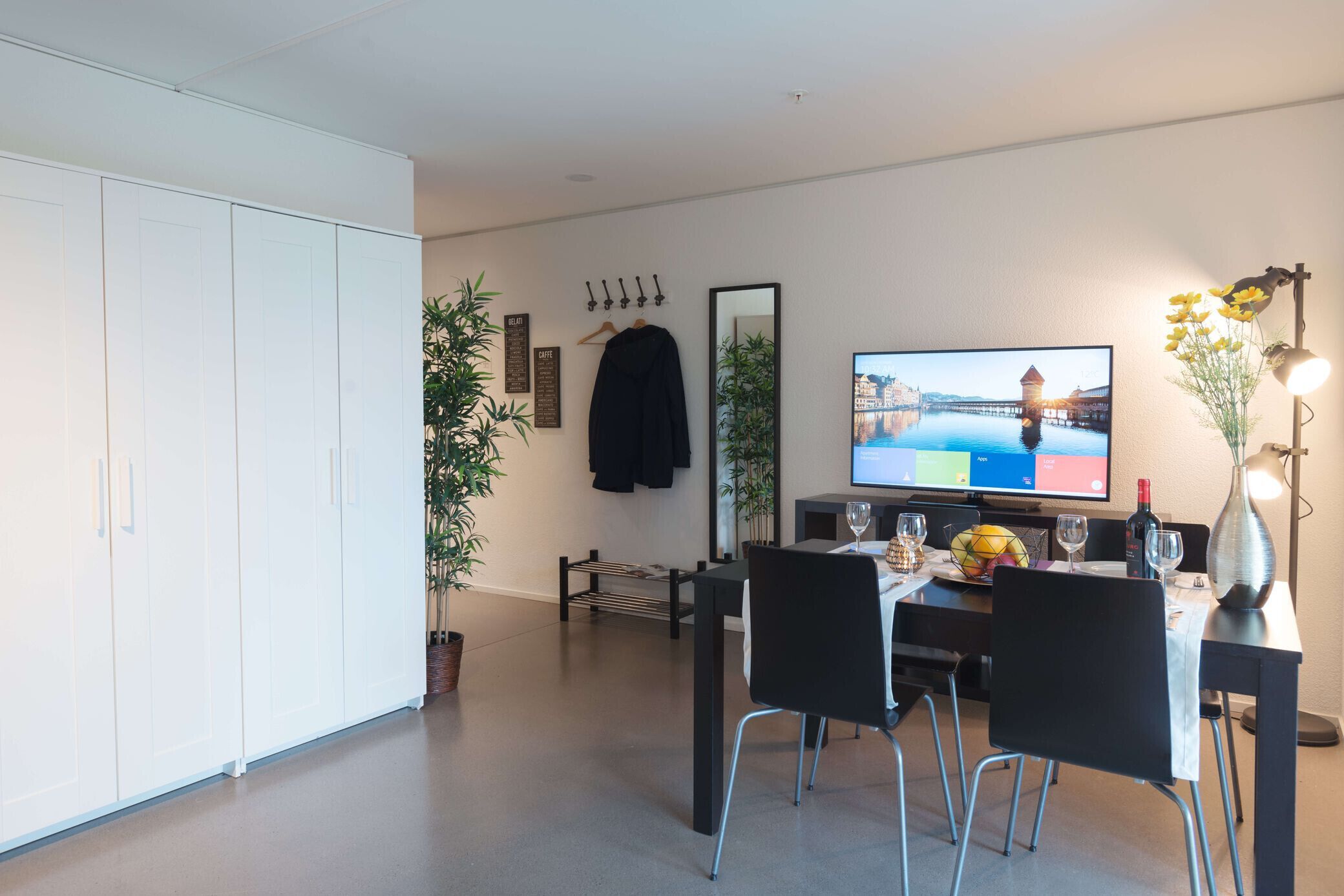 A modern dining area with a table set for two, a television displaying a scenic view, and a plant in the corner.