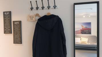A black jacket hanging on a wooden hanger, a wall-mounted sign listing various coffee types, and a framed picture of a car on a bed.