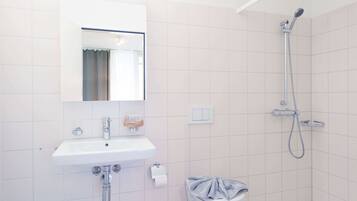 Un baño con lavamanos, espejo y ducha blancos.