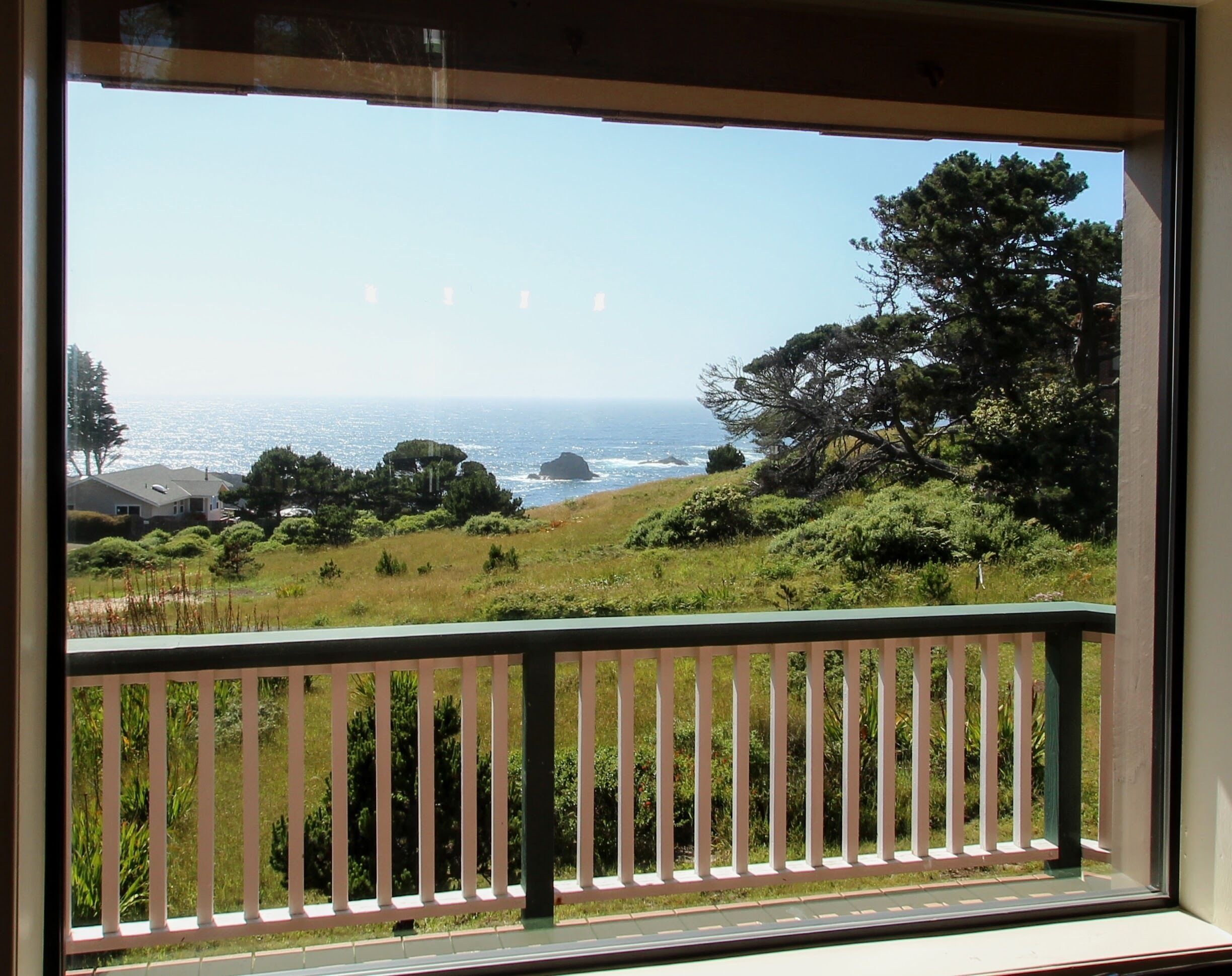 A balcony with a view of the ocean and a grassy landscape.