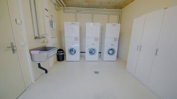 A laundry room with three stacked washing machines, a sink, and a trash can.