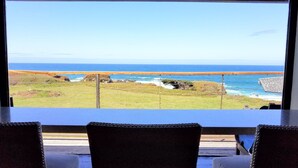 A view from a room with a large window overlooking a coastal landscape, including a grassy area and the ocean. - Star House Lodge - Ocean Front Timbered Lodge (Fort bragg)